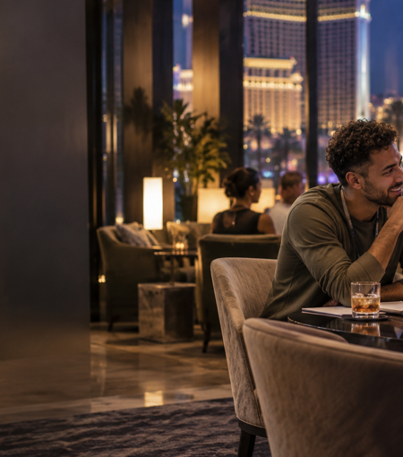 Two colleagues discussing work at a table with a laptop in a modern lounge overlooking a city at night