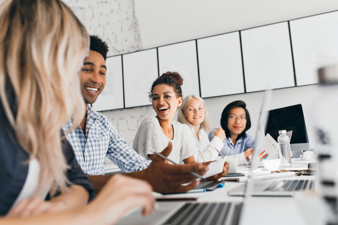 International Employees Sitting in Office With Laptops Talking About Work and Smiling